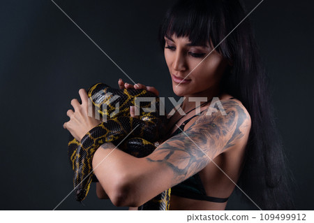 Photo of brunette woman holding yellow anaconda in shadows Photo of brunette woman holding yellow anaconda in shadows 109499912