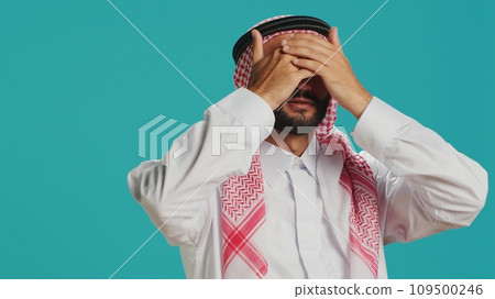 Arab person covers eyes, ears and mouth in studio, presenting three wise monkeys metaphor sign. Middle eastern adult showcasing dont hear, see or speak symbol, muslim costume. 109500246