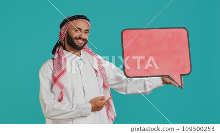 Muslim adult holds speech bubble on camera, creating advertisement for new web commercial. Young person working on marketing industry with empty cardboard icon, isolated billboard sign. Muslim adult holds speech bubble on camera, creating advertisement for new web commercial. Young person working on marketing industry with empty cardboard icon, isolated billboard sign. 109500253