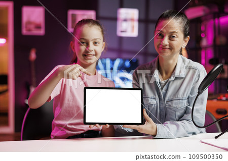 Daughter and mother being sponsored by partnering brand to do mockup tablet unboxing content. Little kid and parent do influencer marketing, doing isolated screen device product placement Daughter and mother being sponsored by partnering brand to do mockup tablet unboxing content. Little kid and parent do influencer marketing, doing isolated screen device product placement 109500350