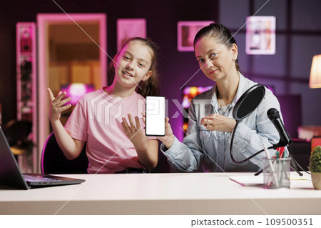 Media star daughter and mother excited to review newly launched mockup smartphone, comparing features with older models. Young internet show host filming video analyzing isolated screen smartphone Media star daughter and mother excited to review newly launched mockup smartphone, comparing features with older models. Young internet show host filming video analyzing isolated screen smartphone 109500351