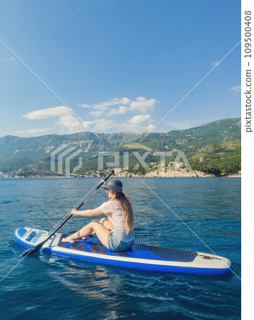 Young women Having Fun Stand Up Paddling in blue water sea near st stefan island against the backdrop of Milocer Park in Montenegro. SUP Young women Having Fun Stand Up Paddling in blue water sea near st stefan island against the backdrop of Milocer Park in Montenegro. SUP 109500408