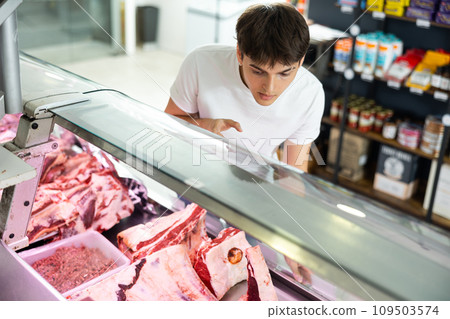 Customer guy near window in meat department of store chooses beef fillet meat for steak Customer guy near window in meat department of store chooses beef fillet meat for steak 109503574