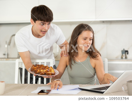 Young guy offering pie to woman working at laptop Young guy offering pie to woman working at laptop 109503764