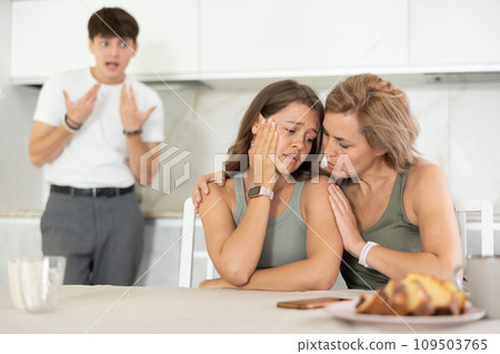 Woman sits near girl and comforts during quarrel with guy Woman sits near girl and comforts during quarrel with guy 109503765