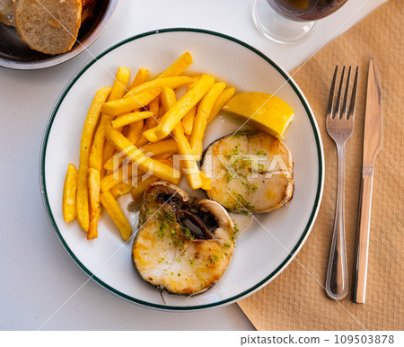 Grilled hake served with potatoes and lemon 109503878