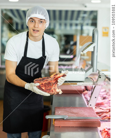 Guy employee of butcher shop cuts meat carcass into small pieces of meat for retail sale in store 109503881