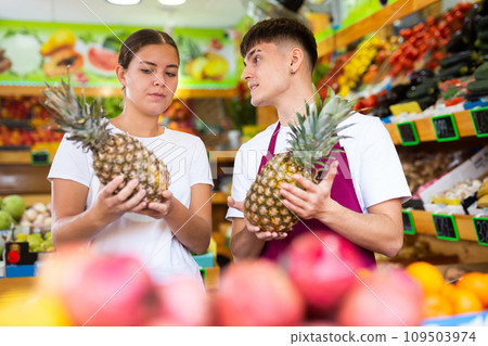 Friendly guy seller helps a girl buyer choose a pineapple 109503974