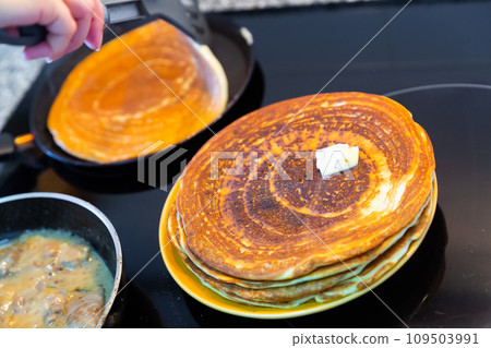 Cook fries thin pancakes in frying pan and places them on plate 109503991
