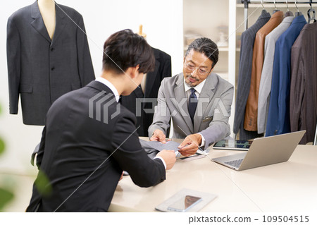 Suit sales staff explaining products while showing fabric samples 109504515