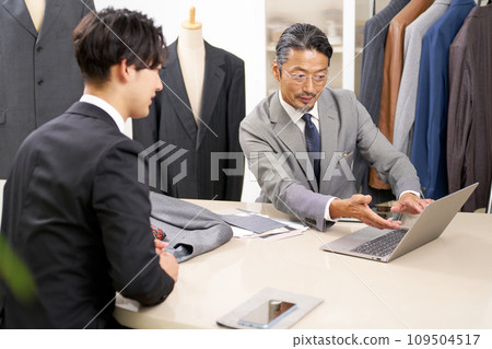 Suit sales staff showing a PC screen to a customer and explaining the product 109504517