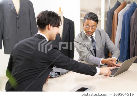 Suit sales staff showing a PC screen to a customer and explaining the product Suit sales staff showing a PC screen to a customer and explaining the product 109504519