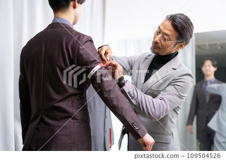 Tailor staff taking customer's measurements in front of the mirror 109504526