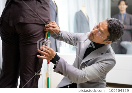 Tailor staff taking customer's measurements in front of the mirror Tailor staff taking customer's measurements in front of the mirror 109504529