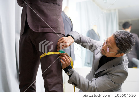Tailor staff taking customer's measurements in front of the mirror Tailor staff taking customer's measurements in front of the mirror 109504530