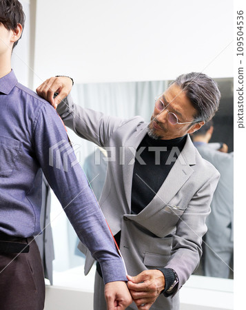 Tailor staff taking customer's measurements in front of the mirror Tailor staff taking customer's measurements in front of the mirror 109504536
