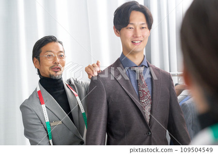 A tailor smiling and talking with a customer in front of the mirror 109504549