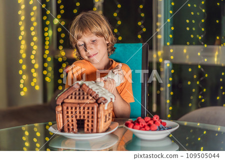 Immerse in festive delight as a boy crafts boy crafting an unconventional gingerbread house, infusing Christmas with unique creativity and festive cheer. A sweet scene of seasonal bonding and culinary 109505044