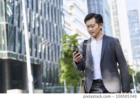 asian corporate executive looking at cellphone while walking in street asian corporate executive looking at cellphone while walking in street 109505348