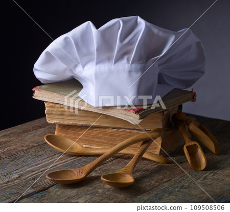 Old culinary books , chef hat and wooden spoons . 109508506