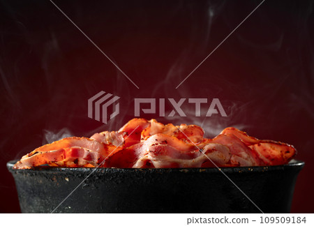 Fried steaming bacon slices in an old black pan. 109509184