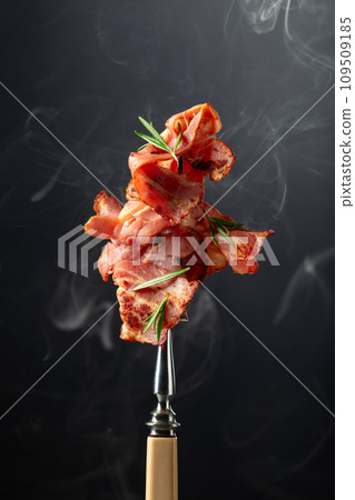 Roasted bacon slices with rosemary on a fork. Roasted bacon slices with rosemary on a fork. 109509185