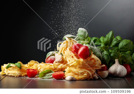 Homemade raw pasta with tomato, garlic, and basil on a black background. 109509196