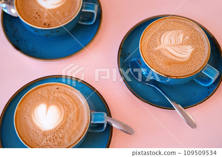 Cup of Cappuccino with Art Milk Foam Top View. Latte with Steel Spoon. Hot Coffee in a Blue Ceramic Mug With Saucer on a Pink Table. Modern Glamour Coffee Shop, Cafeteria. Thick Froth. No People. 4K Cup of Cappuccino with Art Milk Foam Top View. Latte with Steel Spoon. Hot Coffee in a Blue Ceramic Mug With Saucer on a Pink Table. Modern Glamour Coffee Shop, Cafeteria. Thick Froth. No People. 4K 109509534