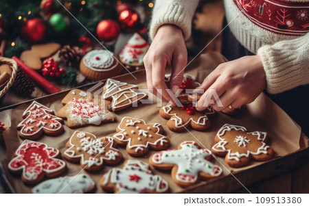 Woman decorating christmas gingerbread cookies with icing sugar on wooden background Woman decorating christmas gingerbread cookies with icing sugar on wooden background 109513380