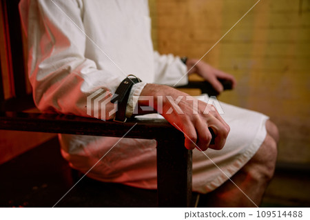 Closeup selective focus on hands of crazy man bound with belt to chair 109514488