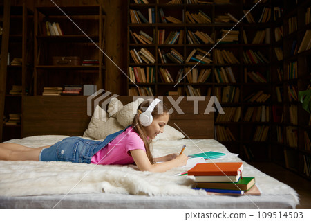 Cute little girl studying at home with wireless headphones Cute little girl studying at home with wireless headphones 109514503