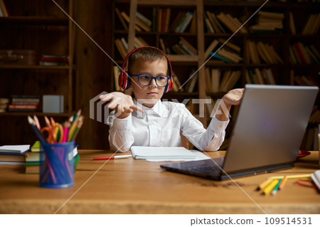 Overwhelmed little schoolboy in headset looking at laptop screen 109514531