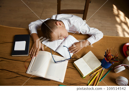 Overhead view on exhausted little schoolboy sleeping on desk table Overhead view on exhausted little schoolboy sleeping on desk table 109514542