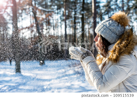Happy woman dressed white sweater and hat blowing snow 109515539