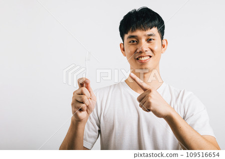 Smiling Asian young man, in a dental health concept, brushes teeth with a toothbrush and points to it with enthusiasm. Studio shot isolated on white background, showing a positive attitude. Smiling Asian young man, in a dental health concept, brushes teeth with a toothbrush and points to it with enthusiasm. Studio shot isolated on white background, showing a positive attitude. 109516654