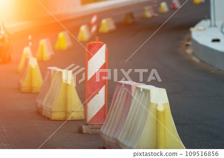 Red, white plastic safety barriers along road. Ensuring road safety with visible barriers. Effective safety measures for roadside work. Red, white plastic safety barriers along road. Ensuring road safety with visible barriers. Effective safety measures for roadside work. 109516856