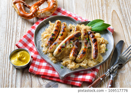 Six fried Nuremberg sausages with sauerkraut on a heart-shaped pewter plate, served with a pretzel Six fried Nuremberg sausages with sauerkraut on a heart-shaped pewter plate, served with a pretzel 109517776