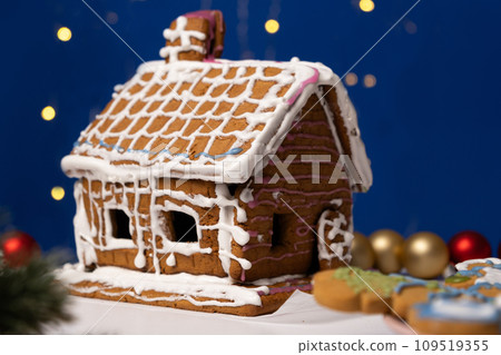 Christmas house made of gingerbread cookies decorated with sugar icing on blue background with bokeh garland Christmas house made of gingerbread cookies decorated with sugar icing on blue background with bokeh garland 109519355