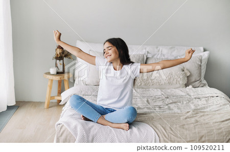 Pre-teen girl in casual clothes do stretching exercises seated on bed in cozy bedroom in the morning 109520211