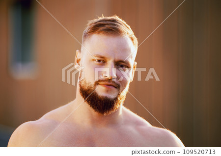 Shirtless broad shouldered bearded white man in his 30s outdoors close up. 109520713