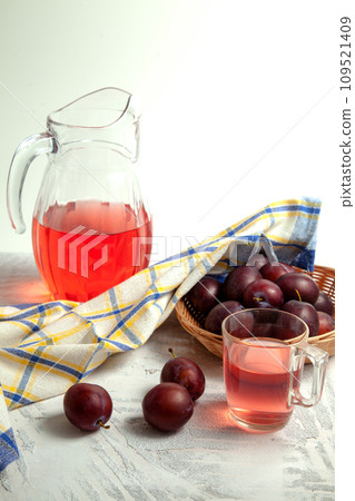 Plum Compote in jug with purple plums on white wooden background. . Plum Compote in jug with purple plums on white wooden background. . 109521409