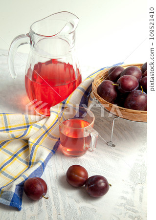 Plum Compote in jug with purple plums on white wooden background. . Plum Compote in jug with purple plums on white wooden background. . 109521410