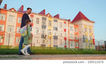 father leads his daughter hand school. happy life family. little child daughter holds happy father hand while going school house. little child and his parent go to class. school life kid with bag his 109522878