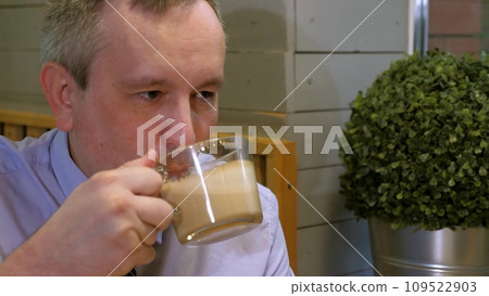 Businessman drinks coffee communicating with partner at meeting in cozy cafe. Businessman takes sip of coffee sitting at table with colleague in cafe. Businessman spends time at informal meeting 109522903