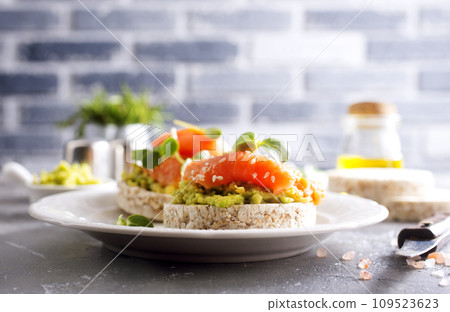 open sandwiches with rye bread, avocado, smoked salmon on a white plate 109523623