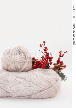 Gray wool skeins or wool yarn with branch of red berries and pine cones on white background. Handmade, knitting, hobby. Copy space. Vertical. Side view 109523748