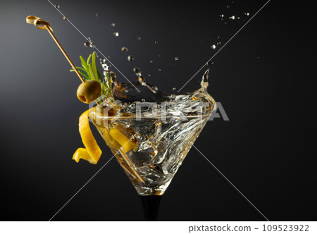 Classic dry martini cocktail with green olives, lemon peel, and rosemary on a black background. Classic dry martini cocktail with green olives, lemon peel, and rosemary on a black background. 109523922