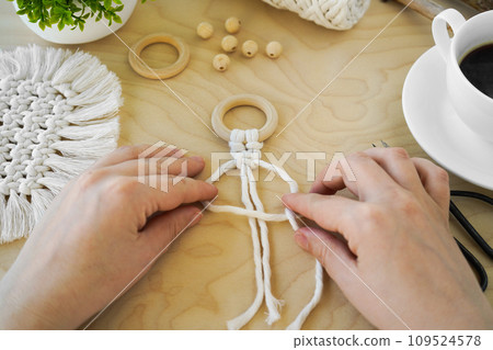 Close-up of women's hands, which are engaged in weaving from natural cotton twine. textile produced using macrame technique Close-up of women's hands, which are engaged in weaving from natural cotton twine. textile produced using macrame technique 109524578