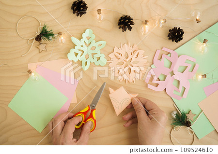 Colorful paper snowflakes cutouts, on a wooden background. Cutting snowflakes from colored paper. Snowflake winter background. Simple winter kids crafts idea. Colorful paper snowflakes cutouts, on a wooden background. Cutting snowflakes from colored paper. Snowflake winter background. Simple winter kids crafts idea. 109524610