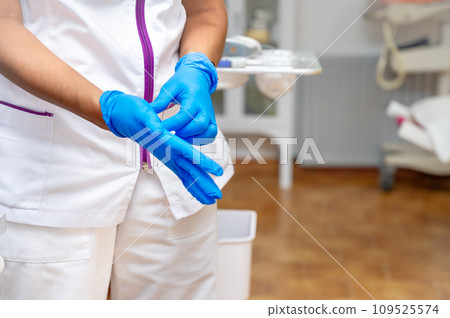 Close up of a female doctor putting a blue latex gloves on a clinic background. Close up of a female doctor putting a blue latex gloves on a clinic background. 109525574